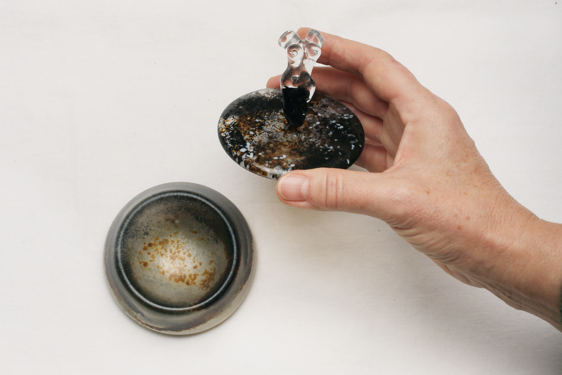 Hand hält Deckel einer Glasdose mit Bugfigur