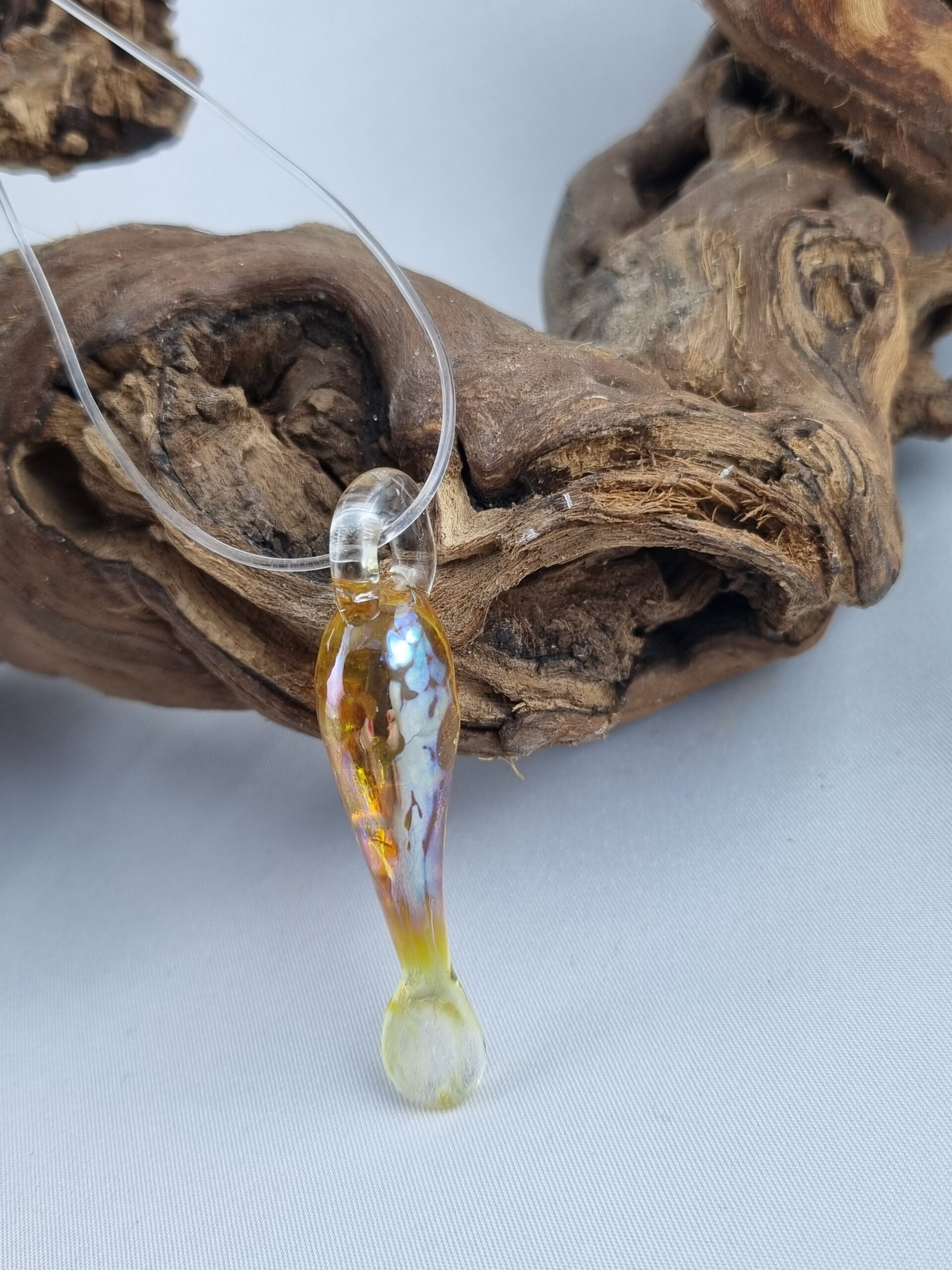 Anhänger minimalistischer Fisch aus gelbgold glänzendem Glas mit klarer Kautschukkette auf Ast