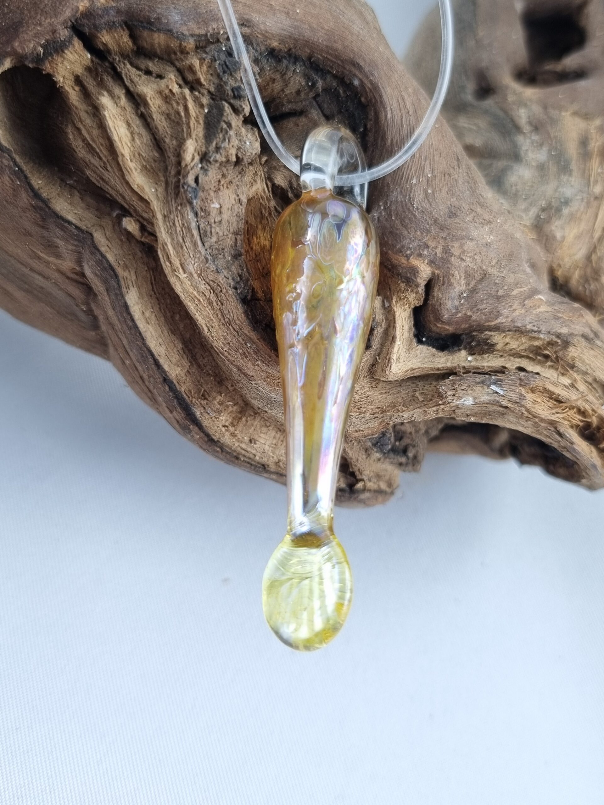Anhänger minimalistischer Fisch aus gelbgold glänzendem Glas mit klarer Kautschukkette auf Ast