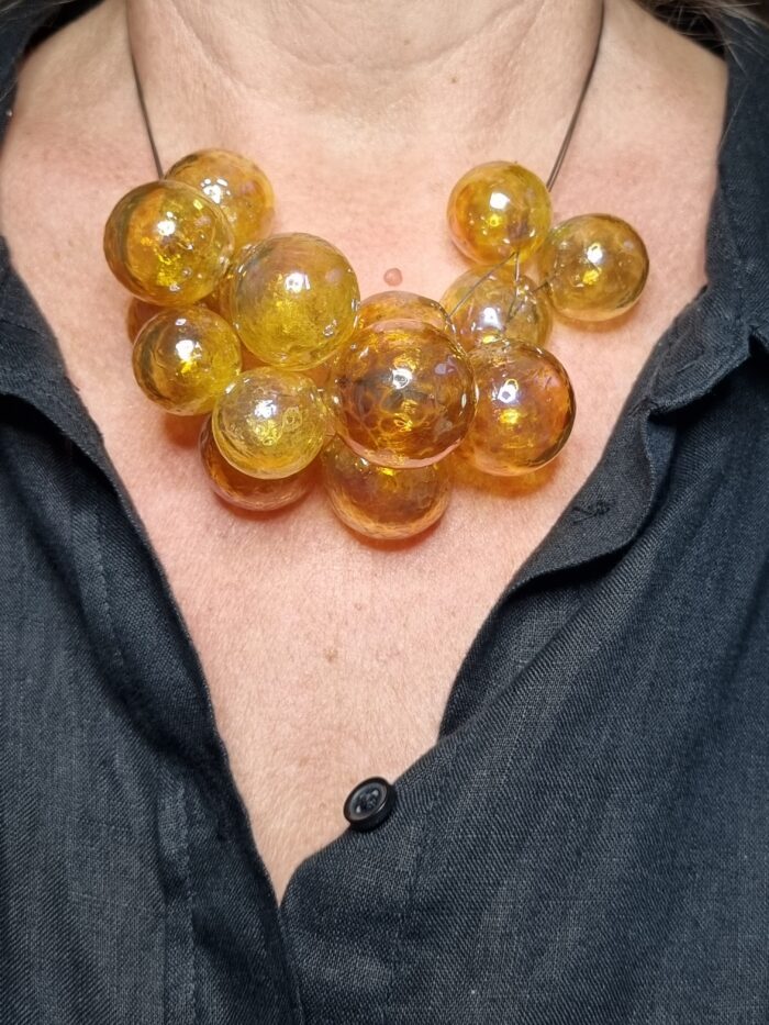 Edelstahlseil mit 15 transparent gelbgolden glänzenden runden Glas Hohlperlen an einem Hals - Tragefoto mit schwarzer Bluse