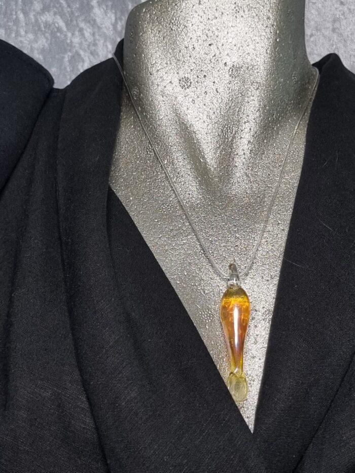 Anhänger minimalistischer Fisch aus gelbgold glänzendem Glas mit klarer Kautschukkette auf Styroportorso, schwarz gekleidet
